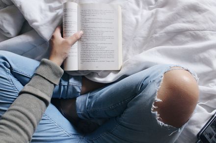 Personne en train de lire un livre, vue de dessus sur son lit, croisant les genoux